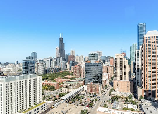 A cityscape with a mix of modern and older buildings, a clear blue sky, and a busy road with cars.