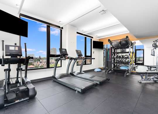 a gym with cardio equipment and windows with a view of the city