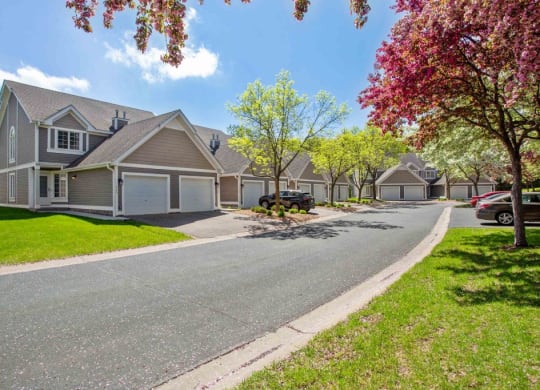 an empty street in front of a row of houses with trees at Seasons Villas, Woodbury, MN 55125