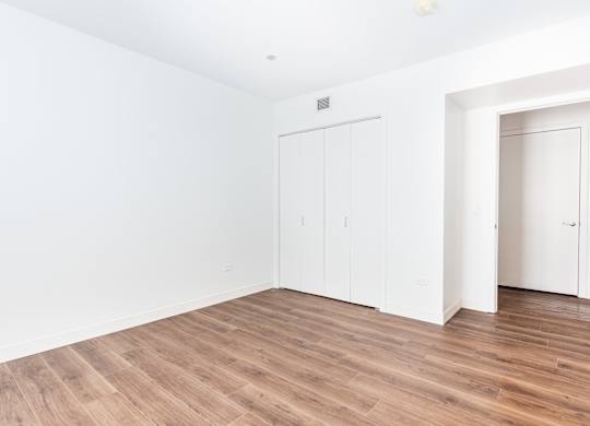 A room with white walls and wooden flooring with two white doors.