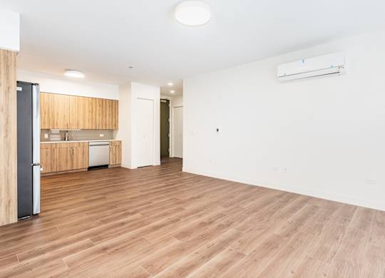 A spacious room with wooden flooring and a kitchen area in the background.