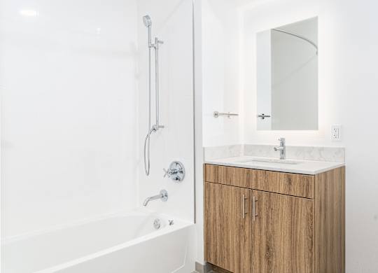 A white bathroom with a wooden cabinet and a white tub.