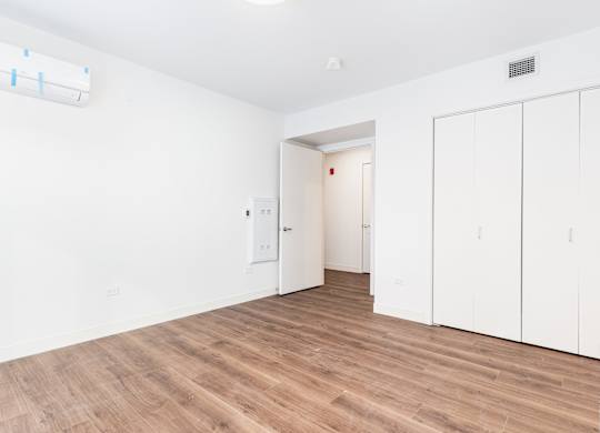 A room with white walls and wooden flooring, featuring a white door and a white cabinet.
