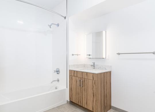 A white bathroom with a wooden vanity and a glass shower stall.