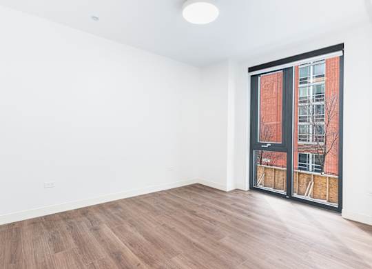 A room with a wooden floor and a window with a view of a building outside.