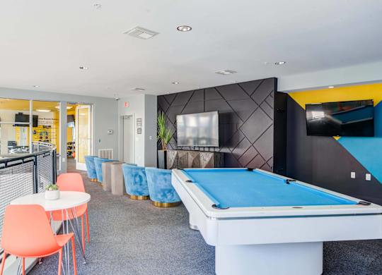 A room with a blue pool table and orange chairs.