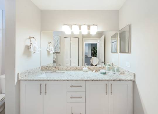 A bathroom with a marble countertop and white cabinets.