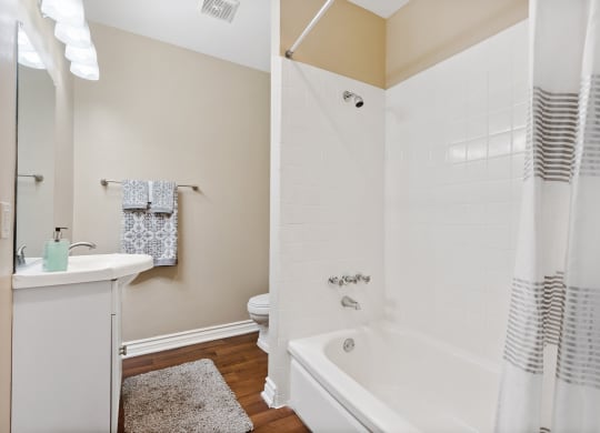 A bathroom with a white tub, sink and hardwood floors at Terramonte Apartment Homes, California