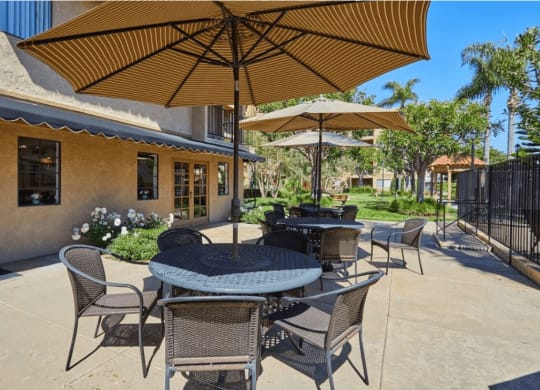 a patio with tables and umbrellas in front of a building at Huntington Terrace North Senior, Huntington Beach, CA