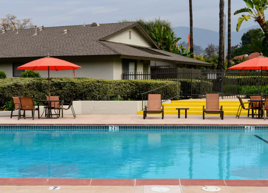 a swimming pool with chairs and umbrellas next to a house at Terramonte Apartment Homes, Pomona