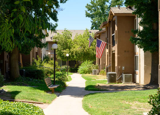 a pathway lined with green grass and trees in front of an apartment building at Oak Terrace Senior Apts, Hemet