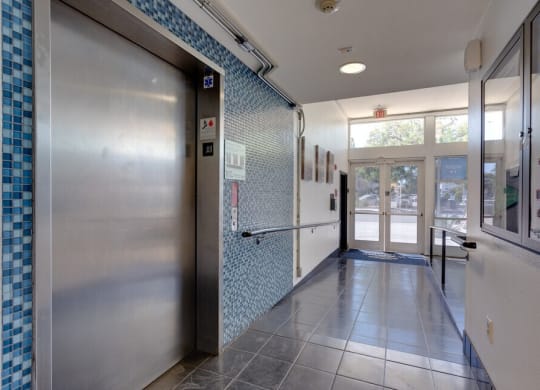 a metal door at the end of a hallway with a blue tile wall at Helix at University Village, Pomona California