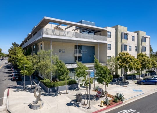 an apartment building with a parking lot and trees in front of it at Helix at University Village, Pomona, CA