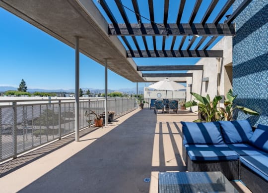 a patio with blue lounge chairs and a white umbrella on a sunny day at Helix at University Village, Pomona, CA 91766