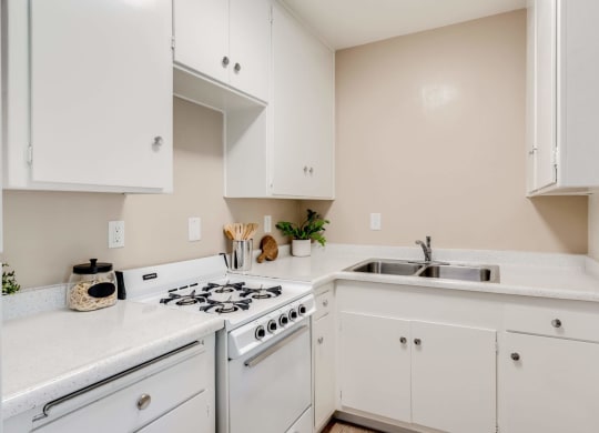a kitchen with white cabinets and a stove and sink at University Park, Azusa, CA