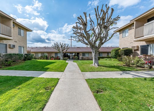 a walkway between two apartment buildings with grass and trees at Colima Terrace Apts, Rowland Heights, 91748