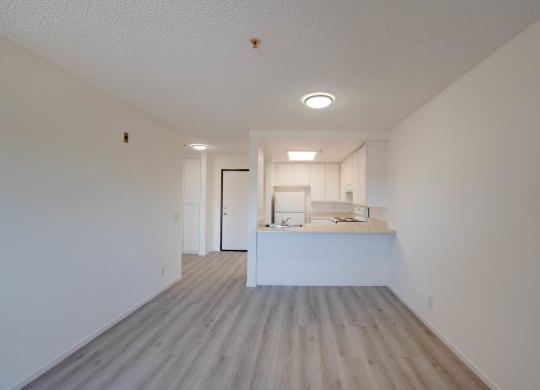 an empty living room and kitchen with white walls and wood floors at Flamingo Garden Senior Apts, El Monte