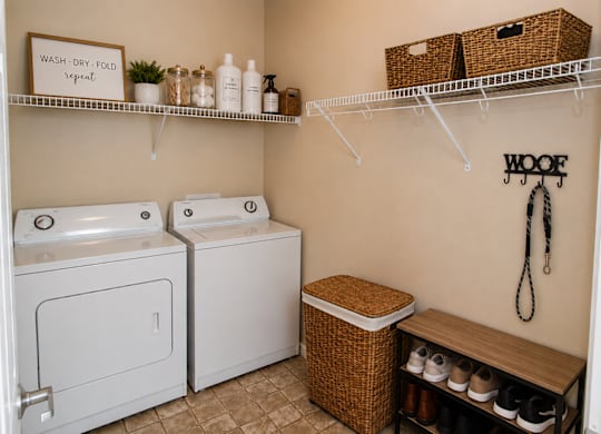 A laundry room with a washer and dryer, a basket, and a shelf with bottles.