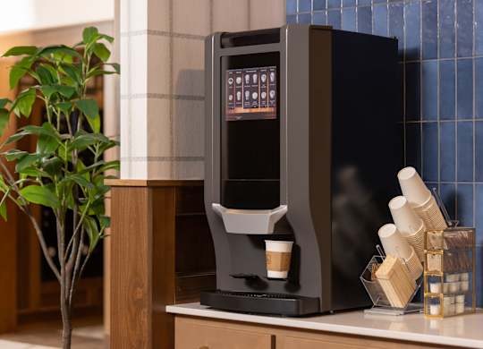 A black coffee machine on a counter with a plant to the left.