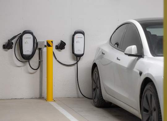 A white car is charging at a yellow charging station.