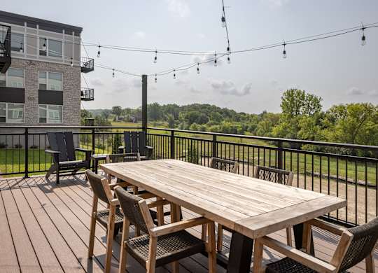 A wooden table with chairs is set up on a deck with a view of a green landscape.