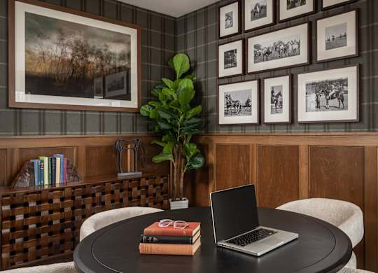 A round table with a laptop and a book on it with a potted plant behind it.