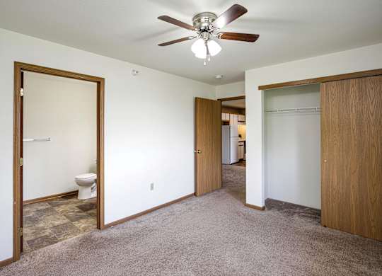 A room with a ceiling fan and a toilet in the bathroom.