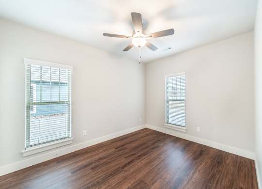 A room with a ceiling fan and two windows.