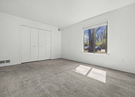 A room with a carpeted floor, a window, and a white door.