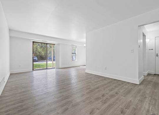 A spacious room with wooden flooring and white walls.