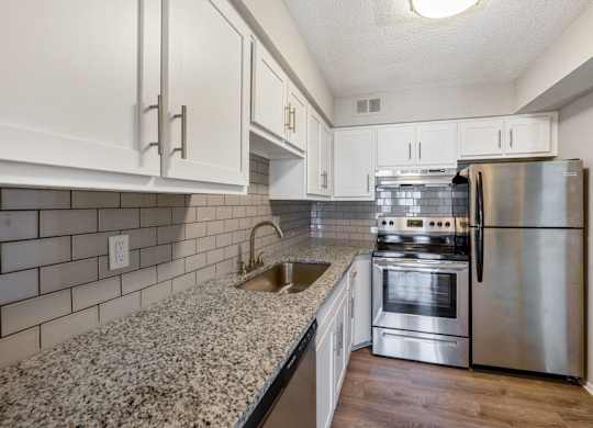 A kitchen with a stainless steel refrigerator, oven, and sink at The Waverly on the Lake - Belleville, MI Apartment , Michigan, 48111