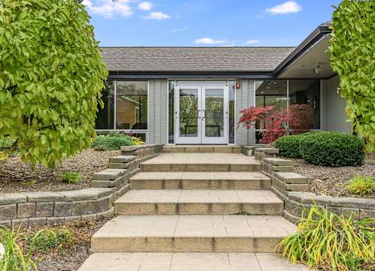 A building with a grey roof and a white door surrounded by green plants at The Waverly on the Lake - Belleville, MI Apartment , Belleville, MI