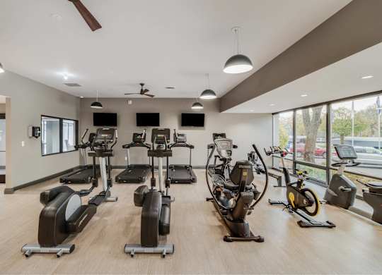 A gym with a variety of exercise equipment including treadmills, stationary bikes, and elliptical machines at The Waverly on the Lake - Belleville, MI Apartment, Belleville, MI, 48111