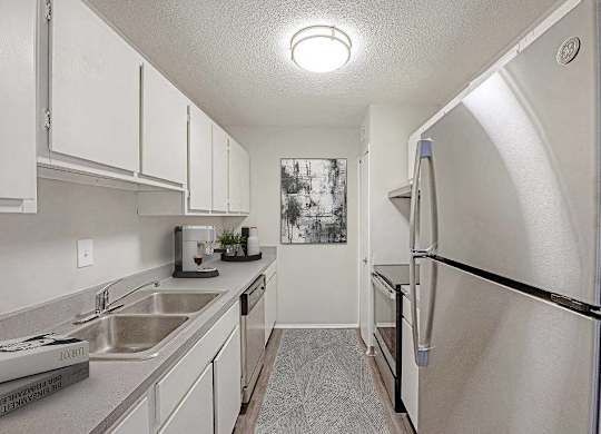 A kitchen with a sink, refrigerator, and cabinets at The Waverly on the Lake - Belleville, MI Apartment , Belleville, 48111