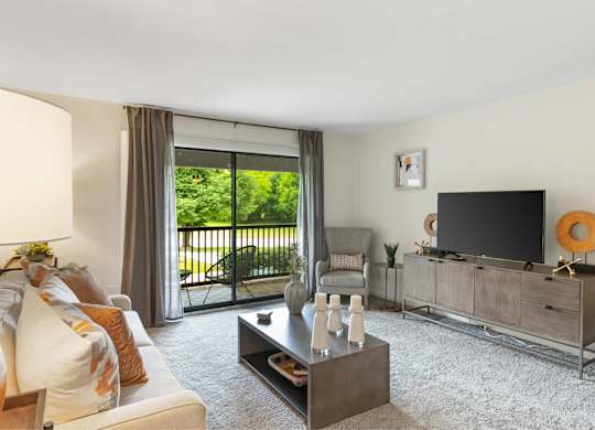A living room with a white couch, a coffee table, a television, and a sliding glass door at The Waverly on the Lake - Belleville, MI Apartment , Belleville