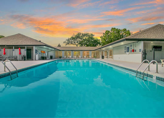 A large swimming pool in front of a building with a sunset in the background at The Waverly on the Lake - Belleville, MI Apartment , Belleville, MI