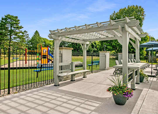 A white pergola is over a patio with a table and chairs at The Waverly on the Lake - Belleville, MI Apartment , Michigan