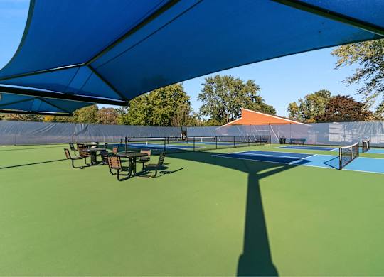 A tennis court with a blue canopy and green surface at The Waverly on the Lake - Belleville, MI Apartment , Belleville, 95050