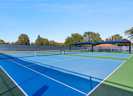 A tennis court with a blue surface and white lines at The Waverly on the Lake - Belleville, MI Apartment , Michigan, 95050