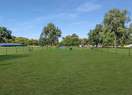 A grassy field with trees and a fence in the distance at The Waverly on the Lake - Belleville, MI Apartment, Belleville, MI, 95050