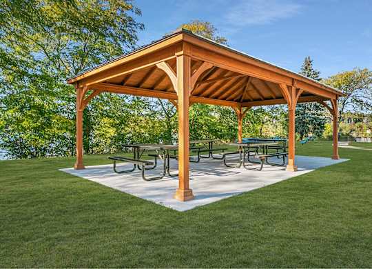 A wooden pavilion with a white base and a roof is surrounded by a grassy area at The Waverly on the Lake - Belleville, MI Apartment, Belleville, MI, 95050