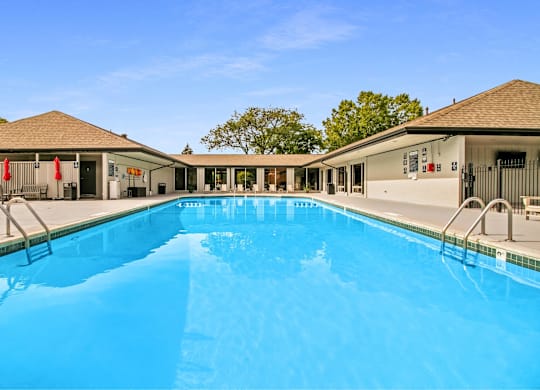 A large swimming pool in front of a building with a clear blue sky above at The Waverly on the Lake - Belleville, MI Apartment , Belleville, 95050