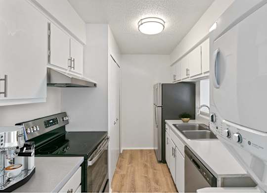 A small, white kitchen with a black stove top oven and a black dishwasher at The Waverly on the Lake - Belleville, MI Apartment , Michigan