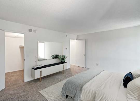 A bedroom with a bed, a mirror, and a bench with a plant on it at The Waverly on the Lake - Belleville, MI Apartment, Belleville, MI, 95050