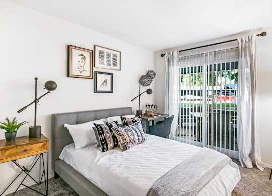 A bedroom with a bed, a nightstand, and a window with a view of a balcony at The Waverly on the Lake - Belleville, MI Apartment , Michigan, 95050
