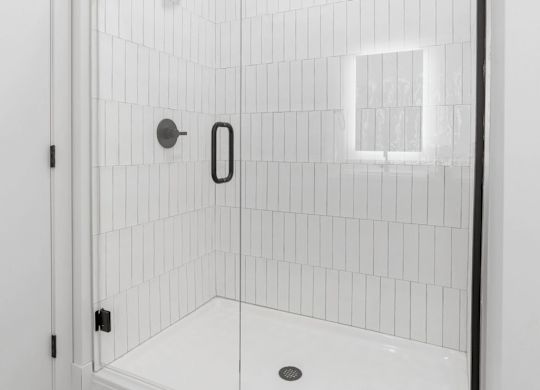 A white tiled shower with a black handle and a black door.
