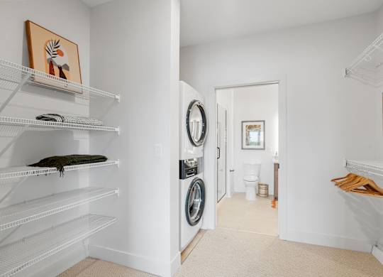 A walk-through closet attached to the bedroom, leading to the bathroom in a one-bedroom, one-bathroom apartment home at Lilia in Lilydale, MN 55118. Features in-unit laundry and storage.