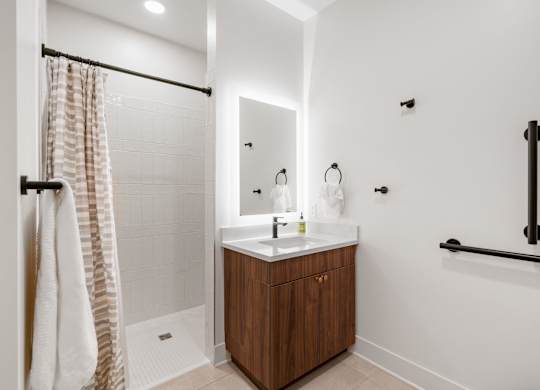 A bathroom with a vanity, backlit mirror, toilet, and walk-in shower in the Guest Suite, a reservable community amenity at Lilia in Lilydale, MN 55118