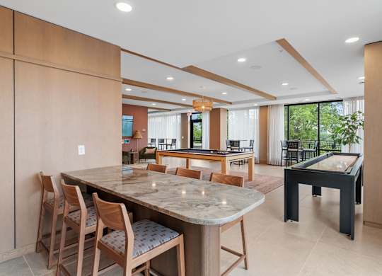 The wet bar overlooking the billiards table, shuffleboard game, and the golf simulator in the Game Lounge, a reservable community room at Lilia in Lilydale, MN 55118