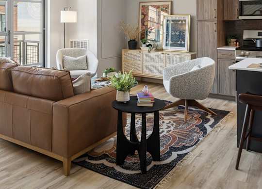A modern living room at The Ellory with a brown leather couch, a white chair, and a black coffee table.